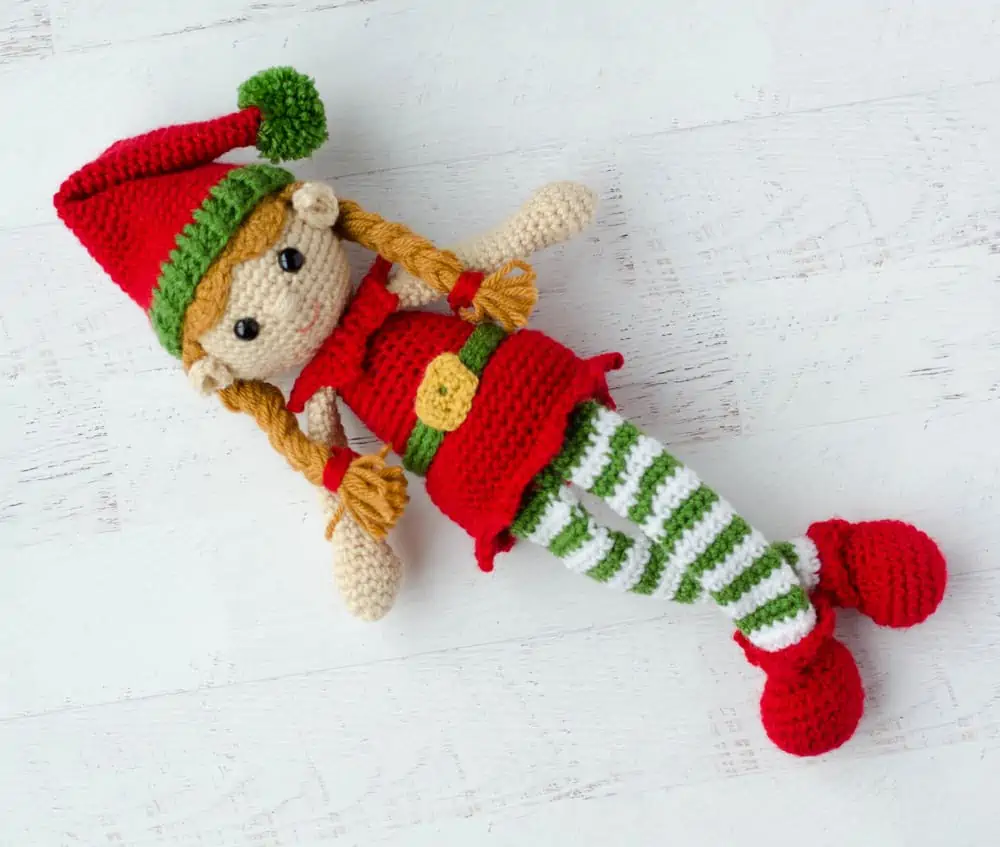crochet elf in red, green and white sitting laying down with legs crossed