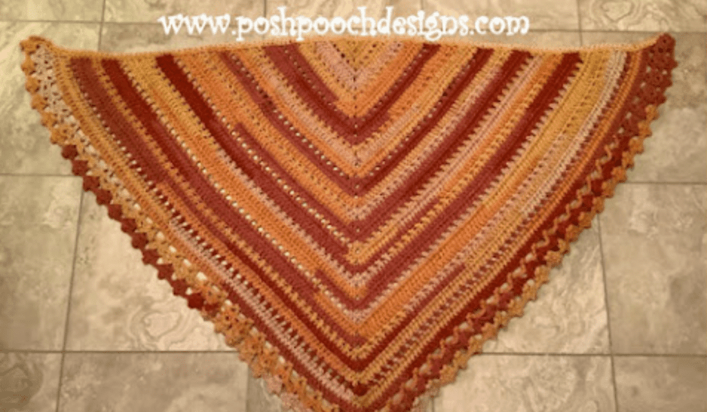 A triangle shawl with yellow, off white, orange, and red yarn.