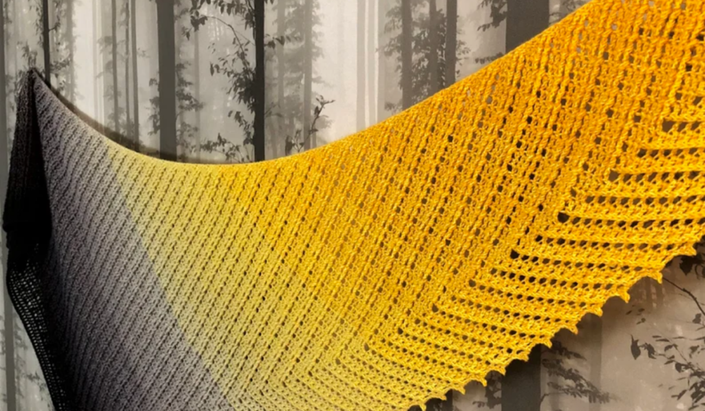 A long, rectangular shawl made with yellow, grey, and black yarn.