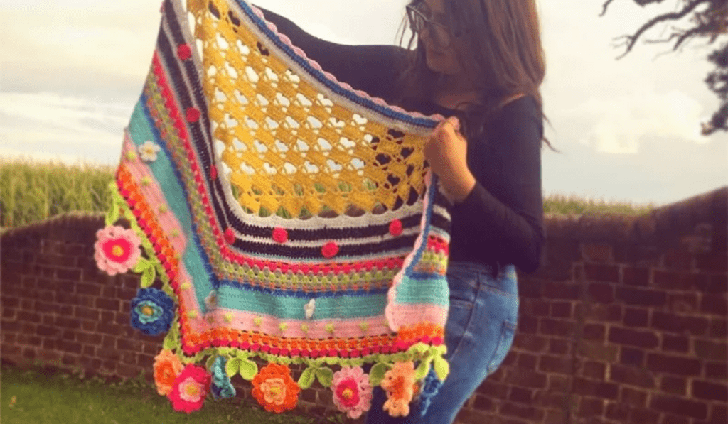 A bright and crazy crochet shawl with different colors and flower motifs throughout.
