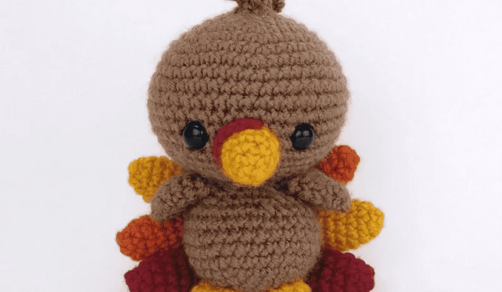 A crochet turkey amigurumi with crochet feathers coming out the back.