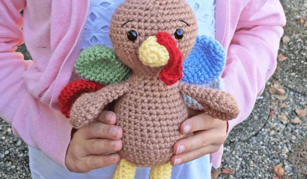 An amigurumi turkey with red, green, and blue crocheted feathers.