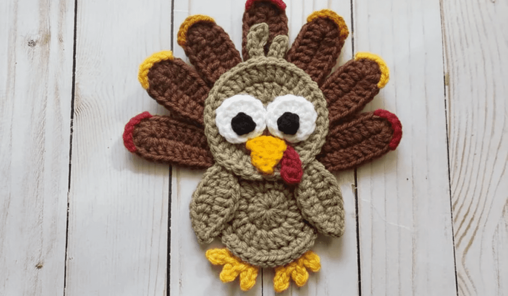 A flat crochet turkey with brown feathers and wings with color at the tips