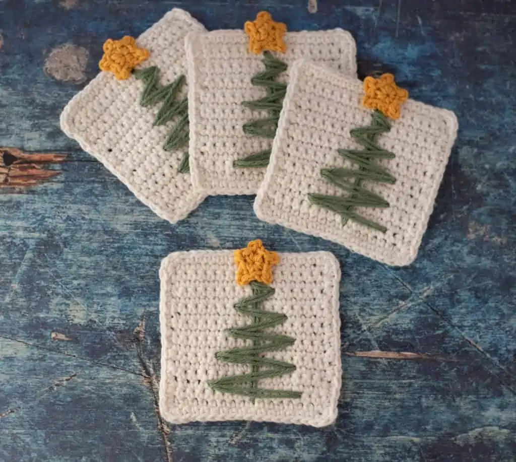 White crochet coasters with green stitched tree and tiny yellow crocheted star