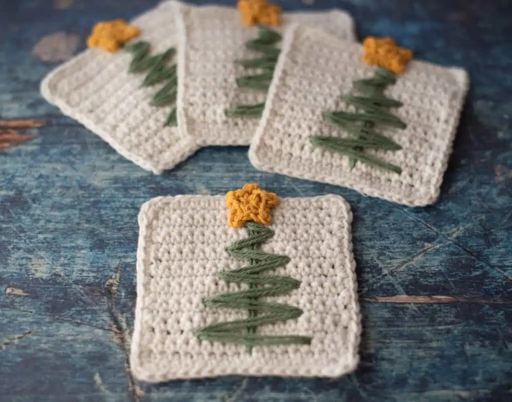White crochet coasters with green stitched tree and tiny yellow crocheted star