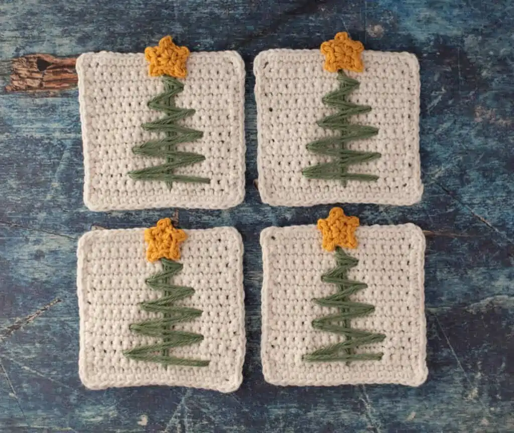 White crochet coasters with green stitched tree and tiny yellow crocheted star