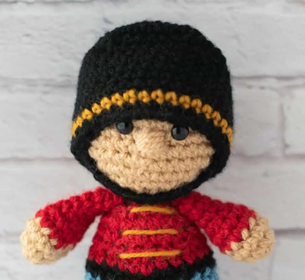 Close up of Crochet nutcracker doll, red shirt with gold trim