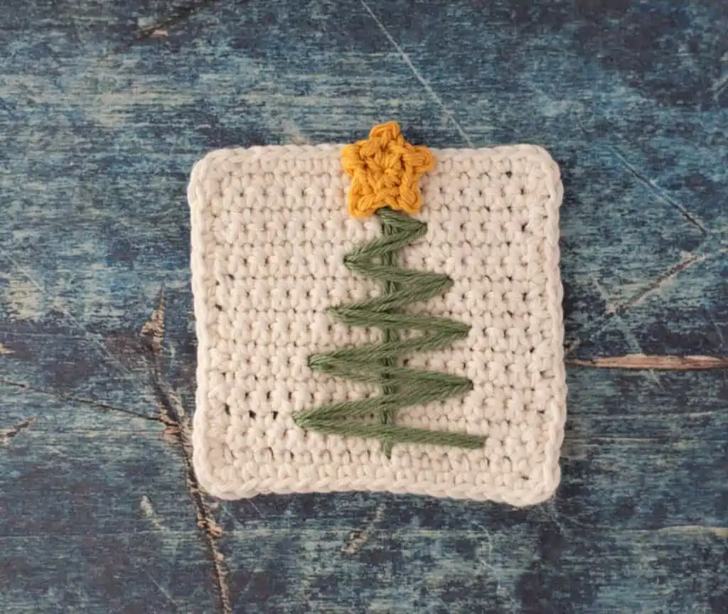 White crochet coaster with green stitched tree and tiny yellow crocheted star