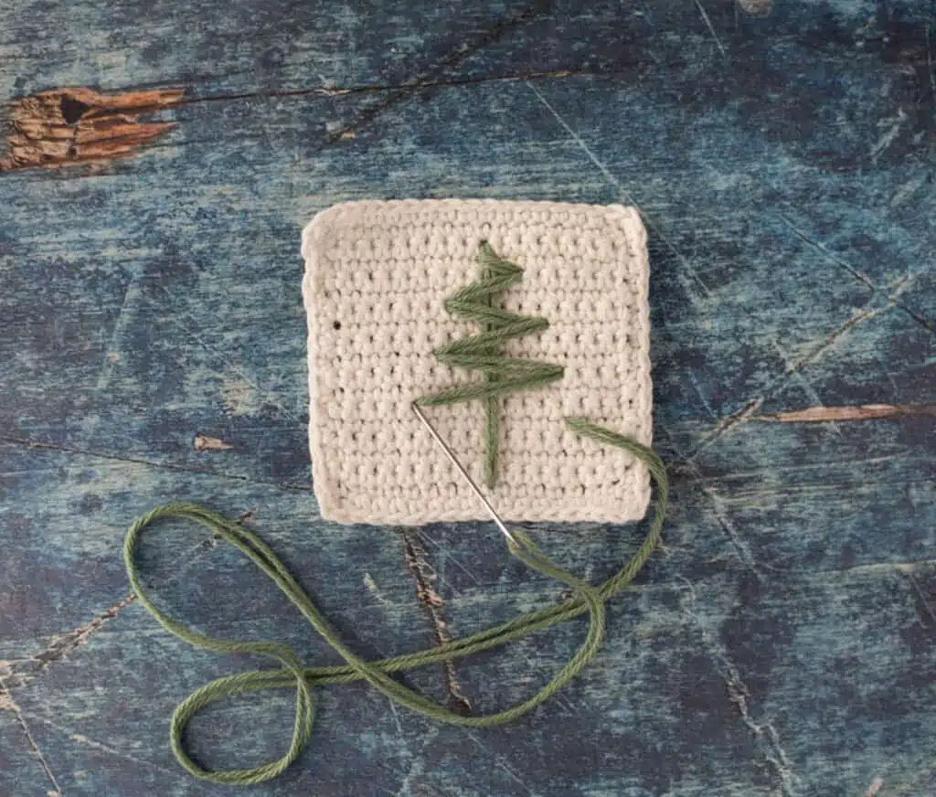 White crochet coaster with green stitching and tapestry needle