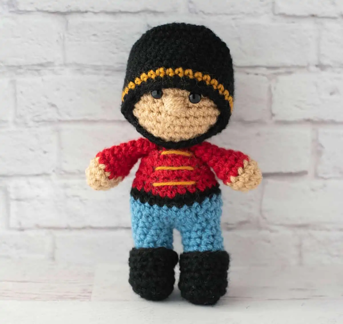 Crochet nutcracker doll, red shirt with gold trim, blue pants, black shoes and ha