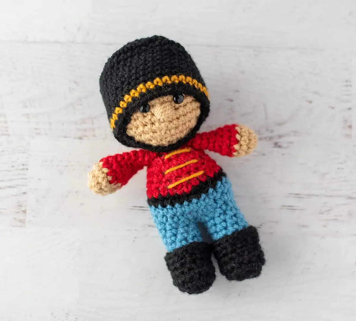 Crochet nutcracker doll, red shirt with gold trim, blue pants, black shoes and ha