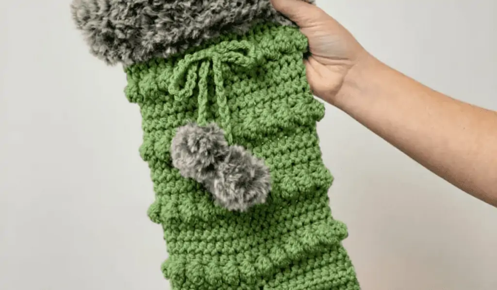 A green crochet stocking with a variety of different stitches to give it texture.
