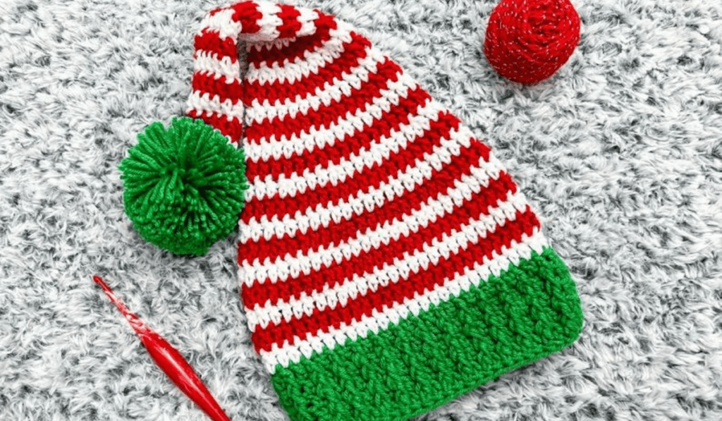 A crochet elf hat with a green brim and red and white stripes of yarn.