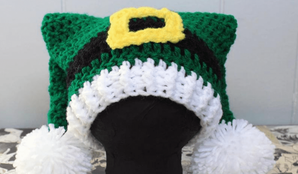 A two-tailed crochet elf hat with a god belt buckle and large white pom poms.