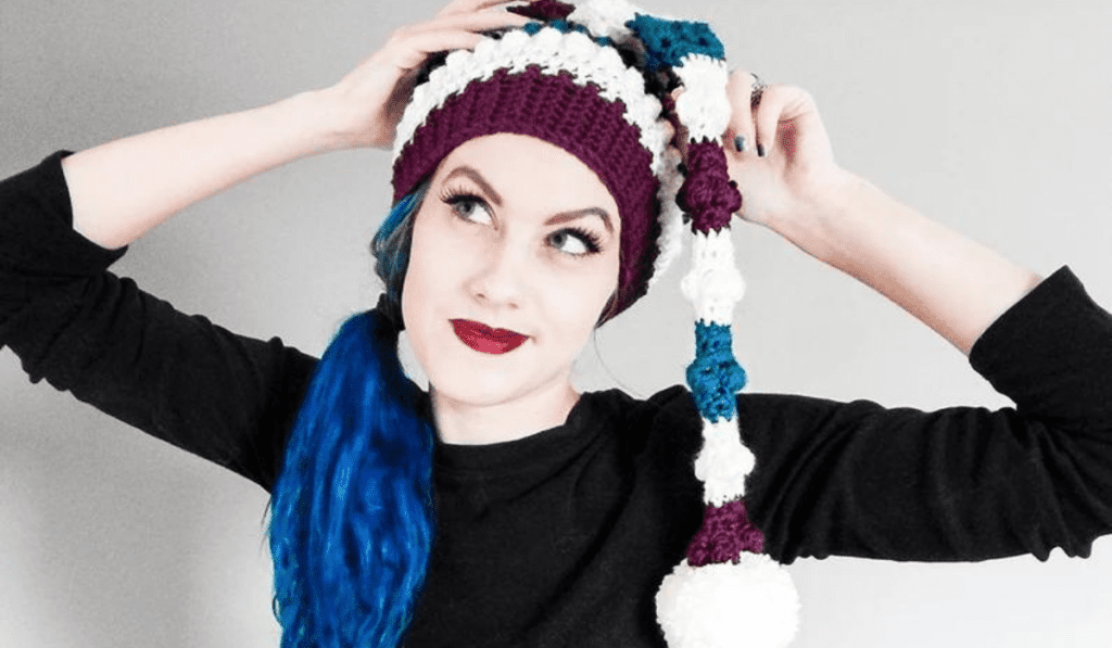 Crochet elf hat with a lot of texture and stripes of purple, white, and blue yarn.