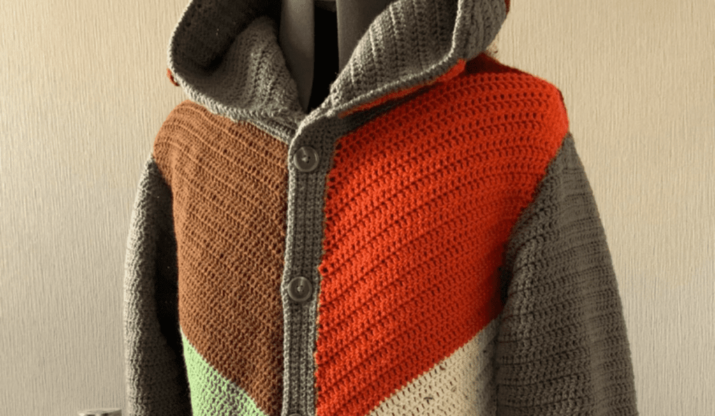 A patchwork crochet sweater with multiple colors and a grey hood.