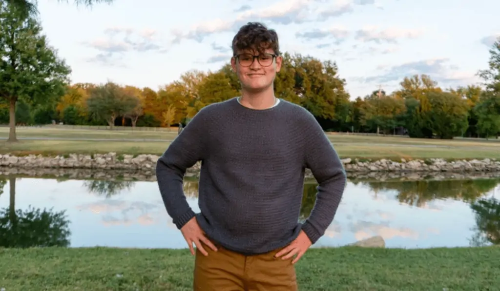 A boy wearing a crochet sweater with a lake in the background