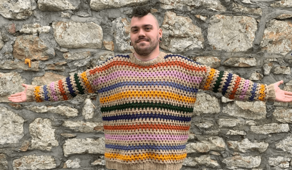 A man wearing a rainbow striped crochet sweater.