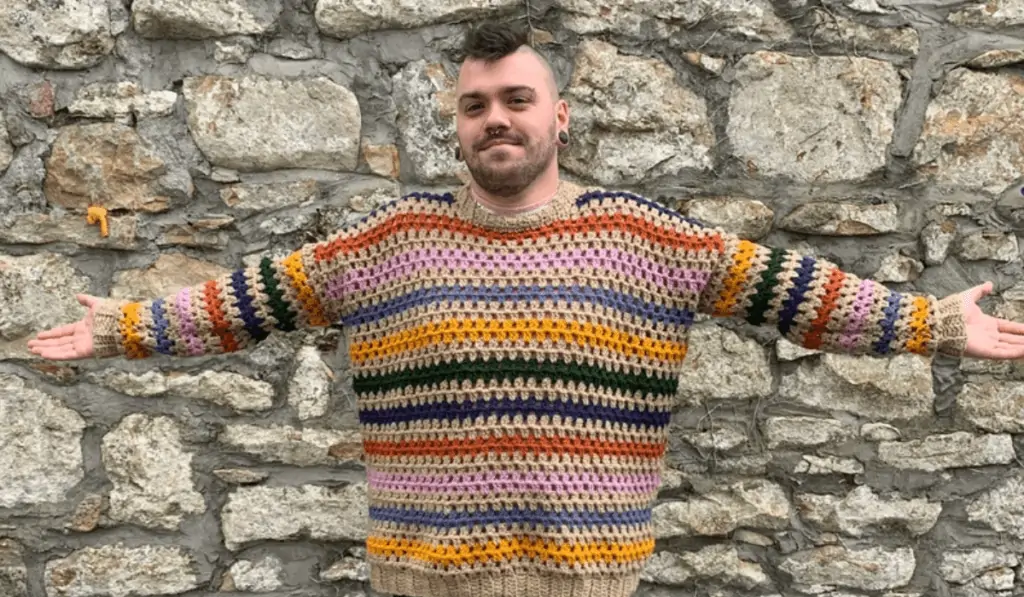 A man wearing a rainbow striped crochet sweater.