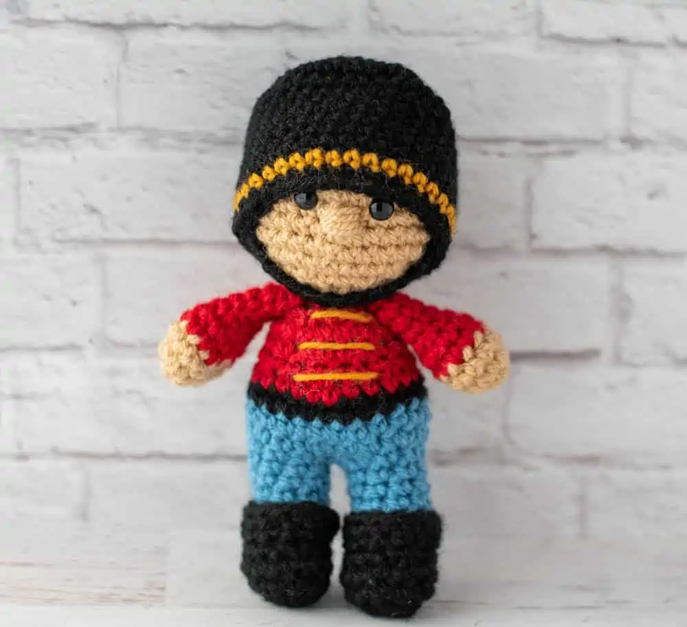 Crochet nutcracker doll, red shirt with gold trim, blue pants, black shoes and ha