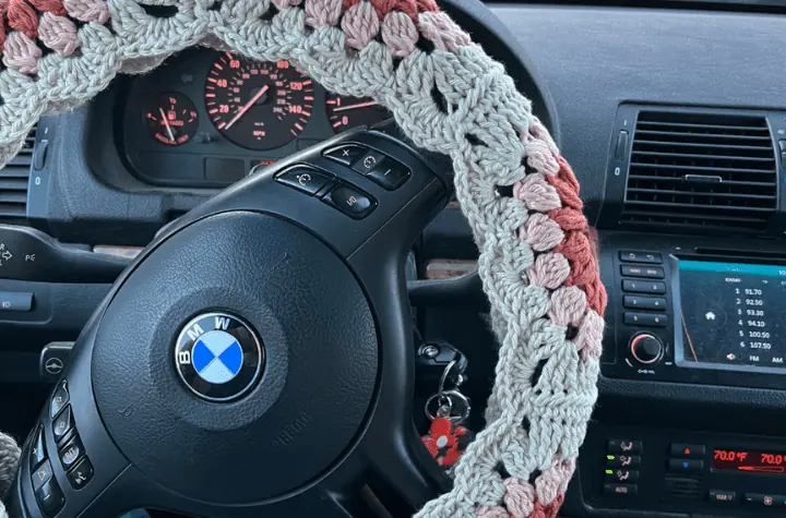 A crochet steering wheel cover featuring pink flowers.