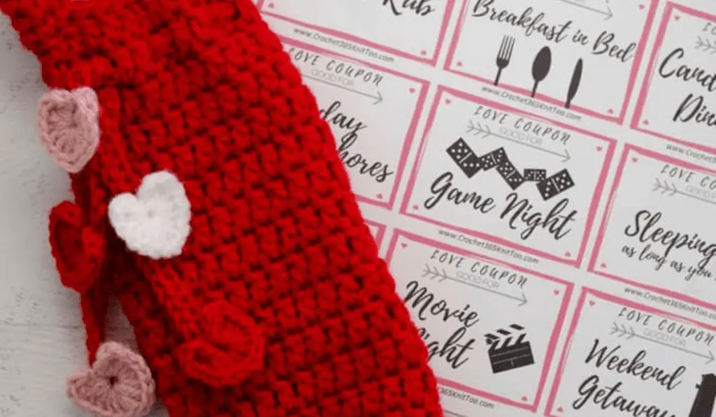 A red crochet wine cozy with little hearts dangling on the side.