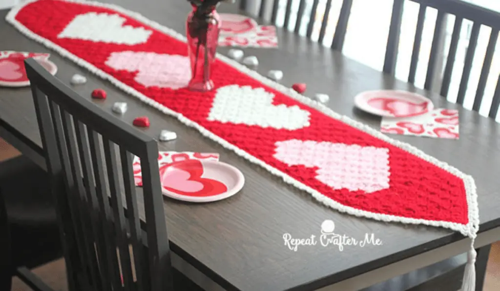 A red crochet table runner with crochet hearts along it on a brown table.