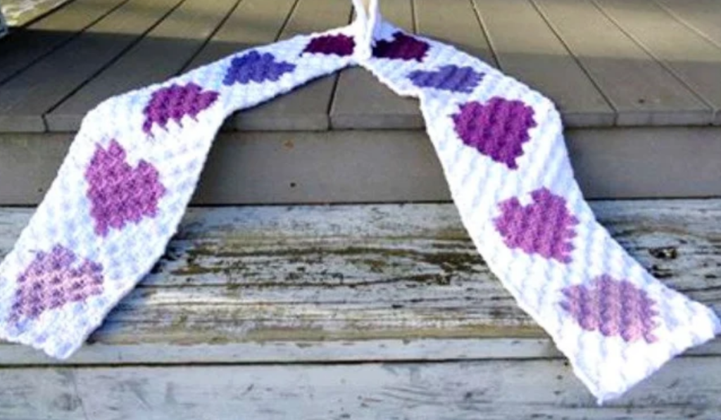 A crochet heart scraf with a variety of purple hearts on it.