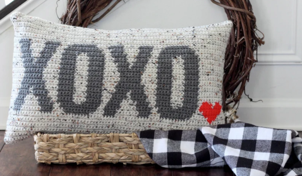 A crochet pillow with XOXO and a small heart on it.