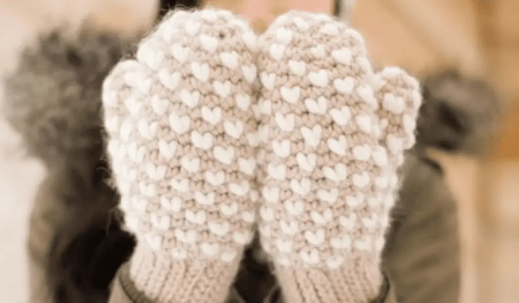 Beige crochet mittens with white hearts.