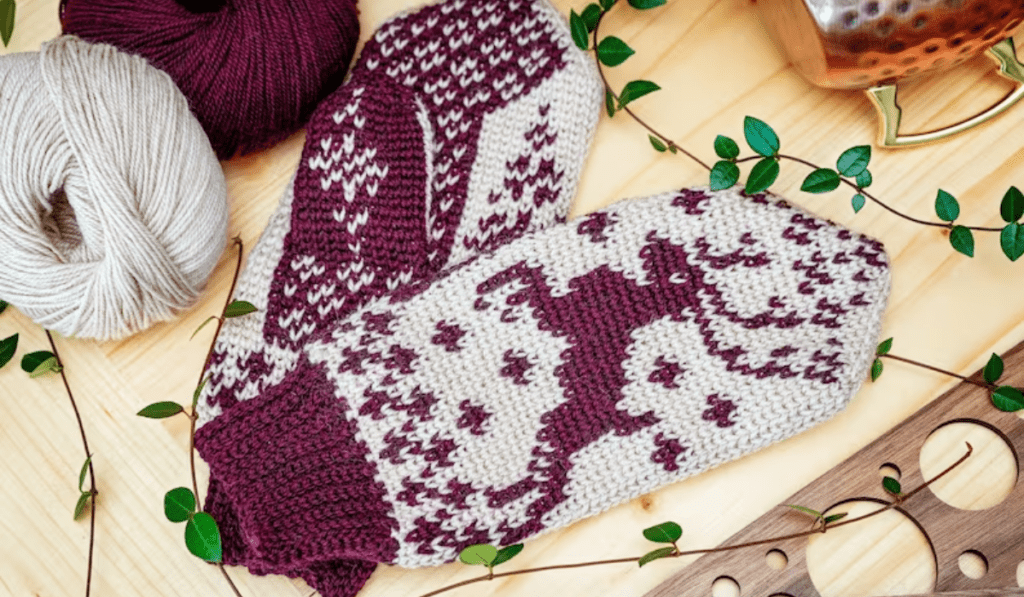 White crochet mittens with purple deer and detailing on the mittens.
