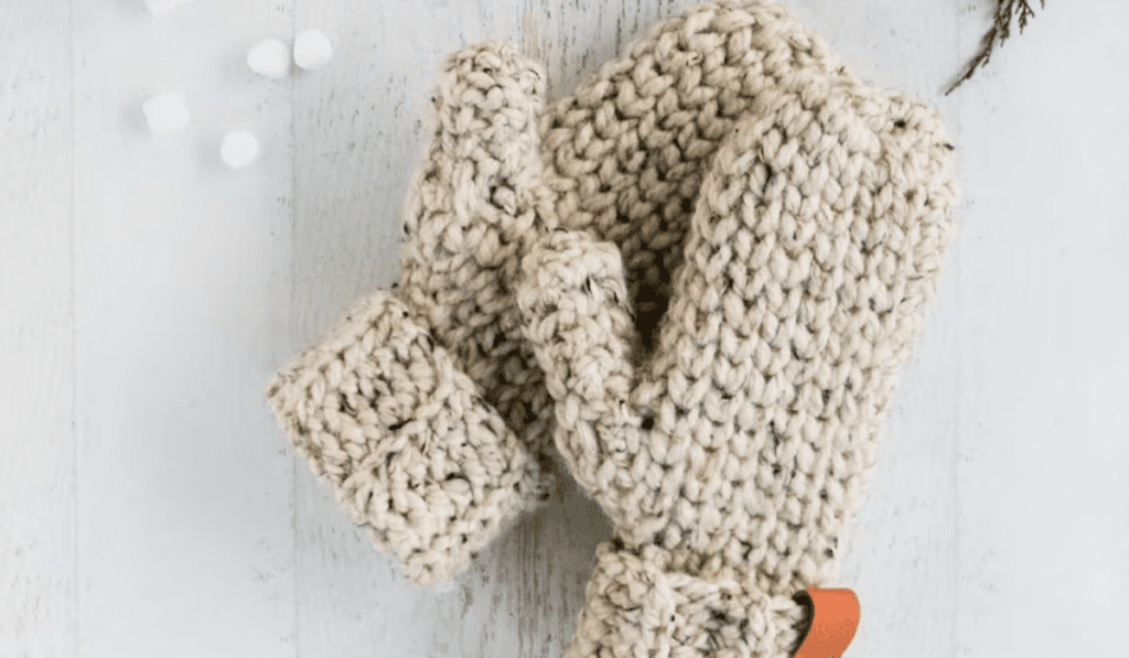Crochet mittens that are off white with black specks.