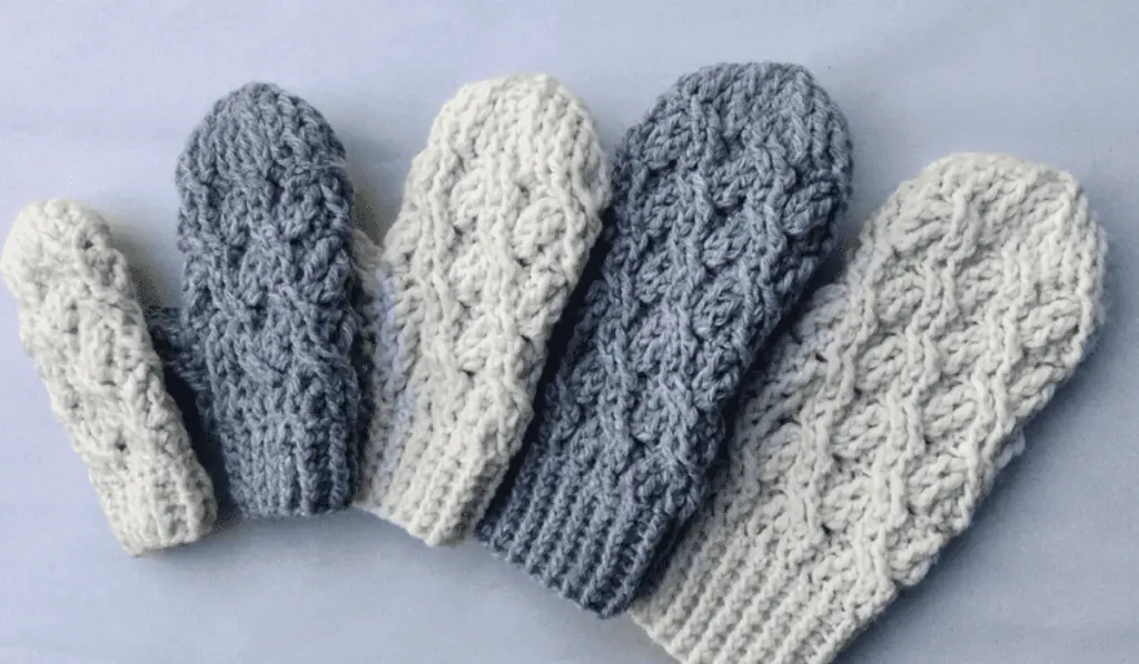 Five crochet mittens in different sizes and lined up from smallest to largest.