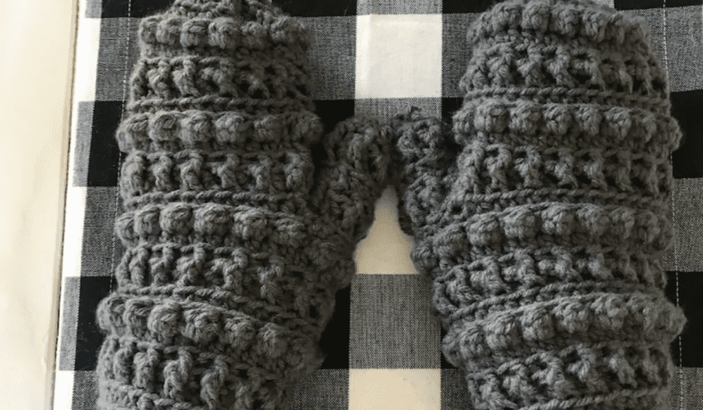 Grey crochet mittens with ball-shaped stitches.