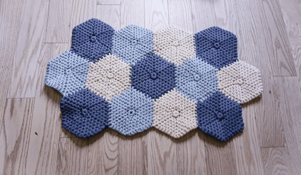 A regtangular rug made up of hexagons in dark blue, light blue, and white yarn.