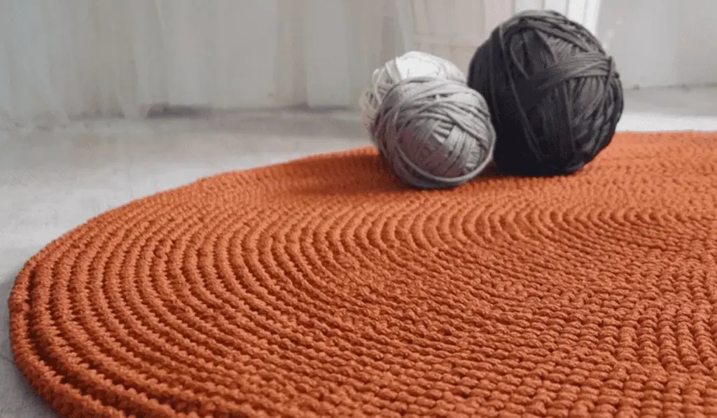 An orange circle rug with three balls of yarn sitting on top in black, grey, and white.