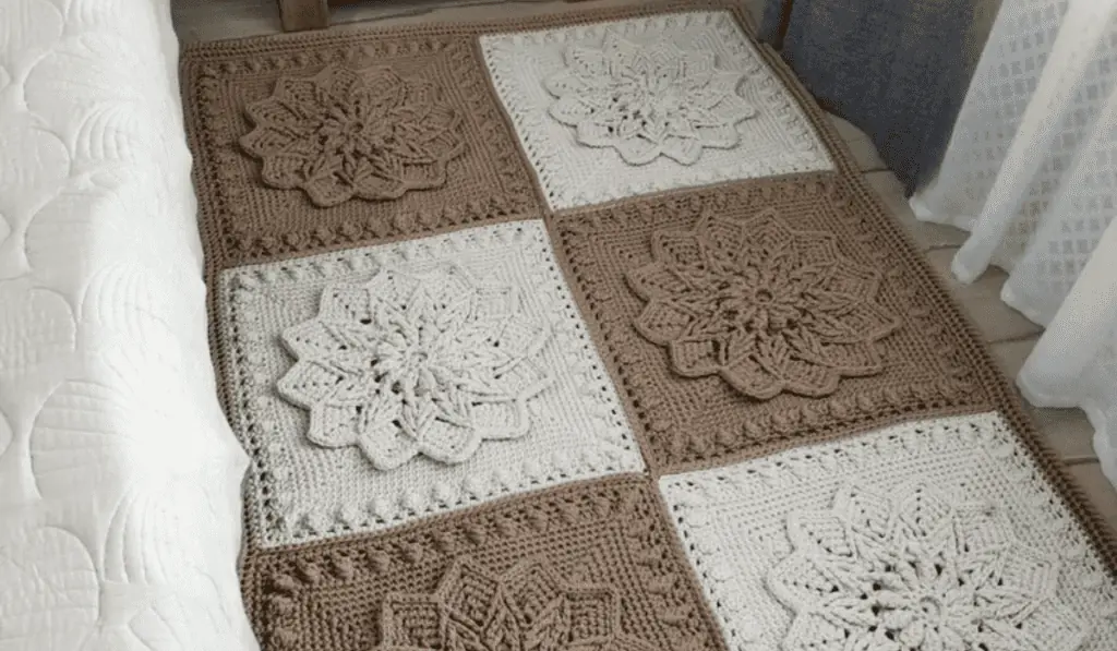 A crochet rug made up of brown and white blocks with little flowers on them.