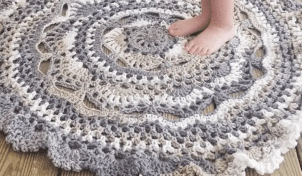 A circular crochet rug made with muted yarn colors, including blue, brown, and white.