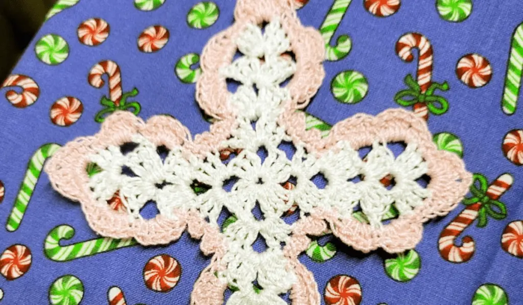 A lacy white cross with a pink border.