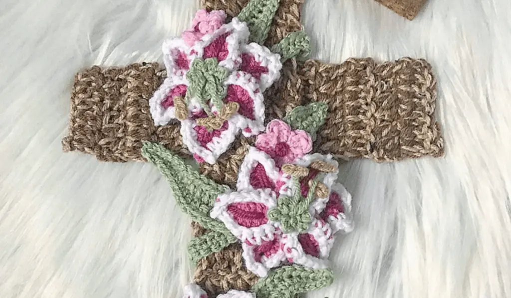 Beige crochet cross with pink flowers along the the center.