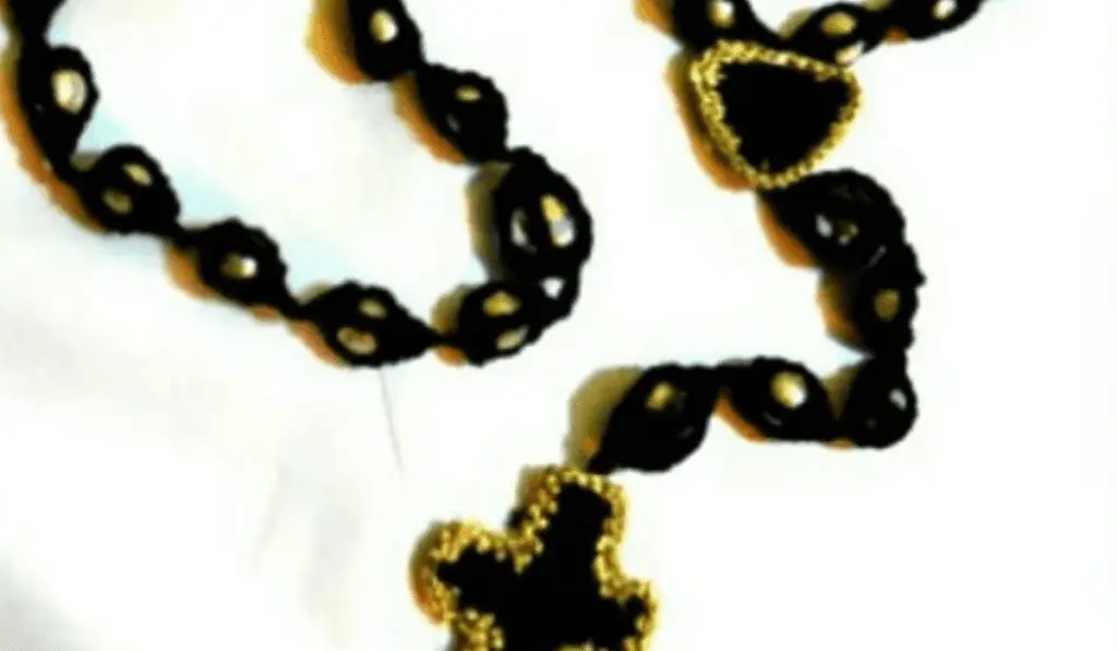 A black crochet rosary that holds the beads in a pocket and a cross at the end with a gold border.