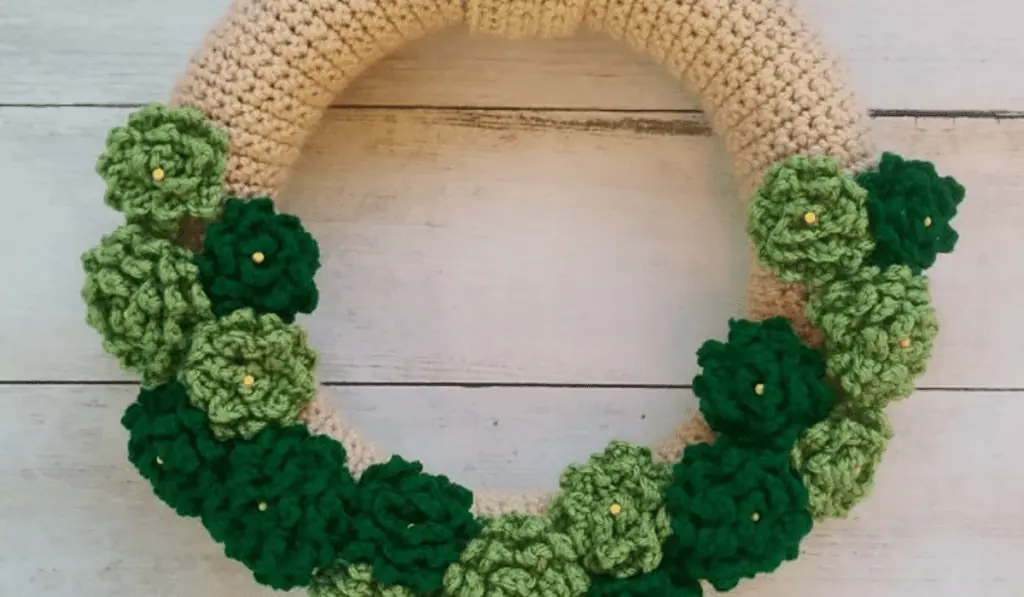 A crocheted wreath with light green and dark green crocheted flowers.