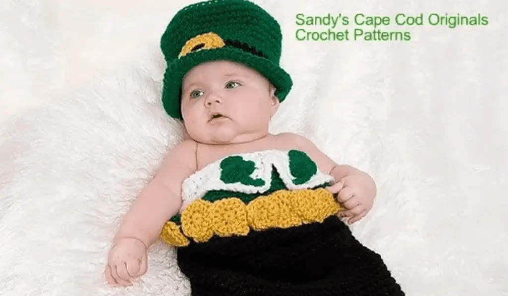 A baby crocheted cacoon that looks like a leprechaun coming out of a pot of gold.