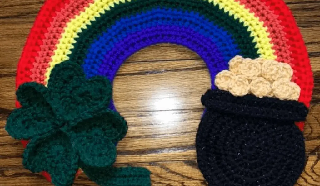A crochet rainbow with a pot of gold on one side and a four-leaf clover.