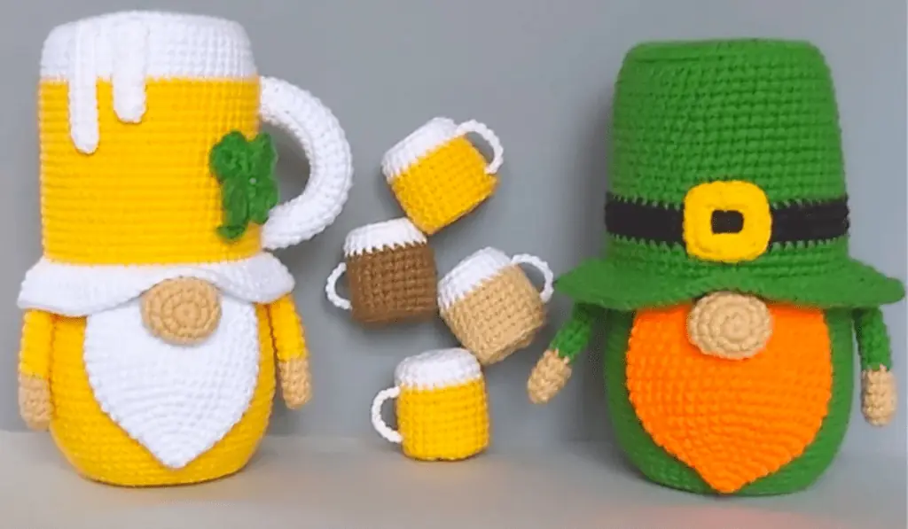 Two gnomes, one that looks like a beer mug and one that looks like a leprechaun with tiny amigurumi beers between them.