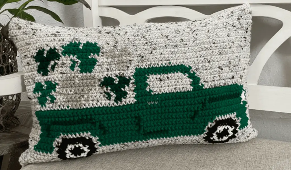 A crocheted vintage green truck pillow with shamrocks in the bed of the truck.