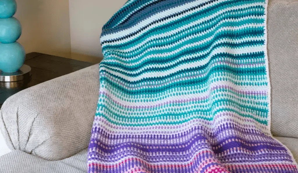 A crochet temperature blanket in blue, white, purple, and pink.