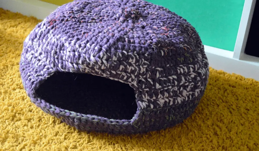 A crochet cat cave bed with purple and white yarn.