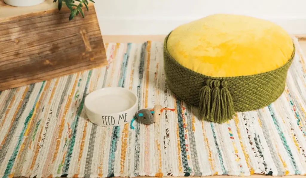A green crochet cat bed with a yellow cushion inside the bed.