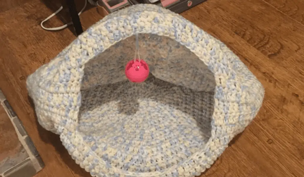 cat-looking crochet cat bed with a toy hanging down from the middle.